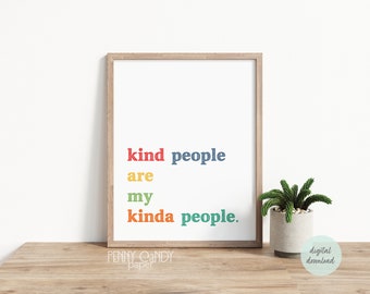 May include: A framed print with the text "kind people are my kinda people." The text is in a rainbow of colors, with the words "kind" and "people" in blue, "are" in yellow, "my" in green, and "kinda" in red. The print is on a wooden table with a small potted plant in the foreground.
