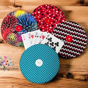 May include: Four round fabric covered boxes with different patterns, including polka dots, zigzags, and a floral design. Each box has a red button in the center. Playing cards are placed on top of the boxes.