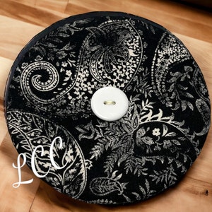 May include: A black and white paisley fabric covered round cushion with a white button in the center.