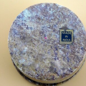 May include: A round, light brown stone box with a dark brown label that reads "MADE IN INDIA".