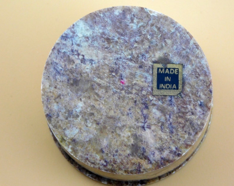 May include: A round, light brown stone box with a dark brown label that reads "MADE IN INDIA".