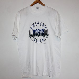 May include: White t-shirt with a blue and black circular graphic that says "Wrigleyville 60613" with ivy vines around the circle.