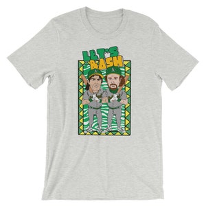 May include: A gray t-shirt with a cartoon illustration of two baseball players in green and yellow uniforms. The text "Let's Bash" is above the players in a yellow box with a green border.