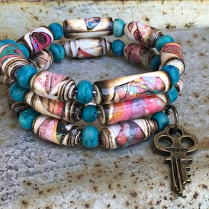 May include: A triple-strand bracelet made of colorful paper beads and turquoise beads with a key charm.
