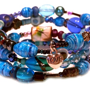 May include: A multi-strand bracelet with blue, turquoise, and black beads. The bracelet features a silver heart charm with the word "LOVE" inscribed on it.