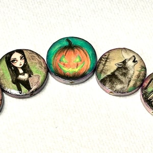 May include: A collection of five round, hand-painted Halloween-themed pendants. The pendants feature illustrations of a black cat in a witch hat, a woman, a jack-o'-lantern, a howling wolf, and a ghost. Each pendant has a purple edge.