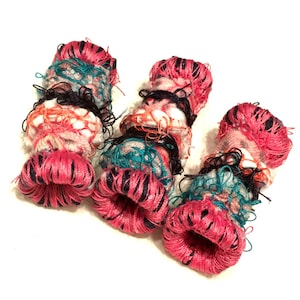 May include: Three colorful fabric covered rings with a pink, black, and teal color scheme. The rings are made of fabric scraps and are hand-stitched.