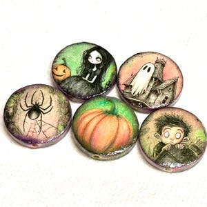 May include: Five round Halloween-themed beads with illustrations. The beads feature a spider and web, a girl with a pumpkin, a pumpkin, a haunted house with a ghost, and a boy. Each bead has a glossy finish.
