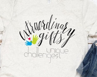 May include: A light beige t-shirt with the words "Extraordinary Gifts, Unique Challenges" in black script. The design includes a colorful hand graphic. The shirt is paired with blue jeans and white canvas sneakers.