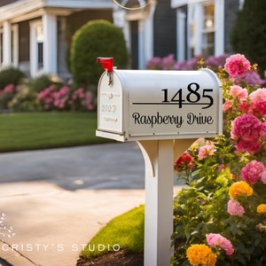 May include: White mailbox with black lettering that reads "1485 Raspberry Drive". The mailbox is mounted on a white post and surrounded by pink, yellow, and orange flowers.