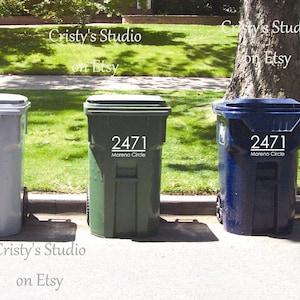 May include: Three curbside trash cans with custom vinyl address numbers and street name.  The cans are gray, dark green, and navy blue. Each can displays the address 