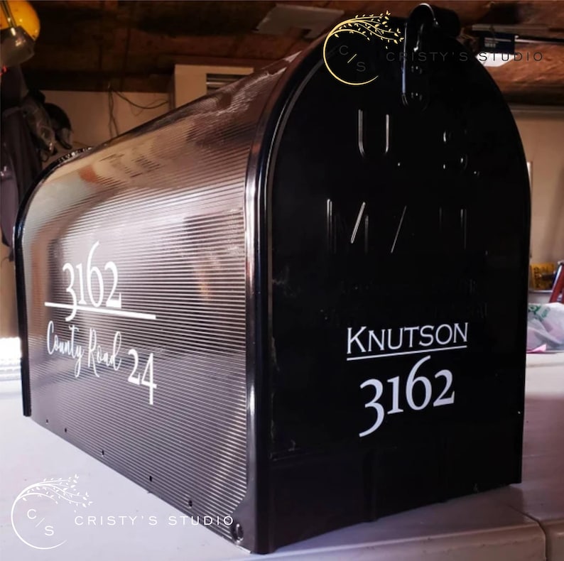 May include: Black mailbox with the address 3162 County Road 24 in white lettering. The mailbox also has the name Knutson and the number 3162 in white. The mailbox has a textured, ribbed design on the front.