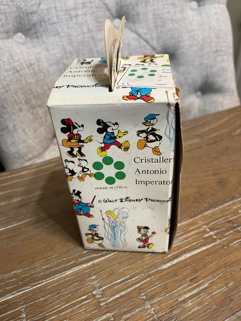 May include: A white cardboard box with a green and red design featuring various Disney characters, including Mickey Mouse, Donald Duck, and a fairy. The box is labeled "Cristaller Antonio Imperatore" and "WALT DISNEY PRODUCTS".