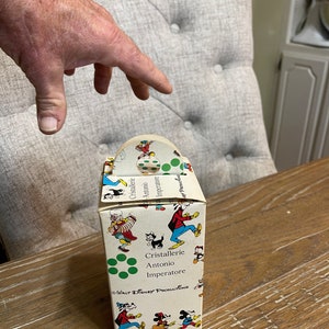 May include: A vintage cardboard box with a handle, featuring a colorful pattern of Mickey Mouse and other Disney characters. The box is labeled "Cristallerie Antonio Imperatore" and "Walt Disney Productions".