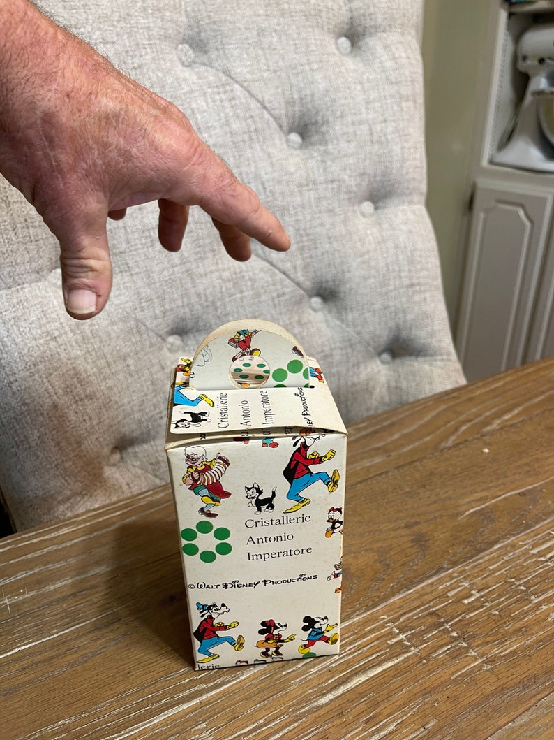 May include: A vintage cardboard box with a handle, featuring a colorful pattern of Mickey Mouse and other Disney characters. The box is labeled "Cristallerie Antonio Imperatore" and "Walt Disney Productions".