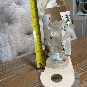 May include: A clear glass figurine of Mickey Mouse holding a musical instrument. The figurine is in a white box with a colorful illustration of Mickey Mouse and other Disney characters. The box also includes the text "Imperatore oggettistica" and "ACC".
