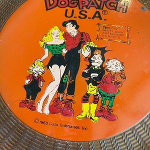 May include: Orange and brown Dogpatch U.S.A. frisbee with a cartoon image of five characters. The text "Good is better than evil because it's nicer!!" is in a wooden sign in the upper right corner. The copyright text "1968 Capp Enterprises Inc." is at the bottom.