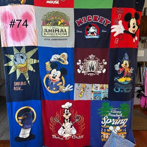 Puede incluir: Una colcha de retazos hecha con varias camisetas con temática de Disney. La colcha presenta a Mickey Mouse, Donald Duck, Goofy y otros personajes de Disney. La colcha es azul, roja, verde y blanca. La colcha está numerada #74.