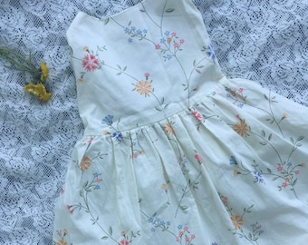 May include: A white dress with a floral print. The dress has a ruffled hem and a sleeveless design.