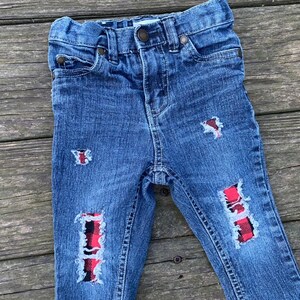 May include: Blue denim jeans with red and black plaid patches on the knees.