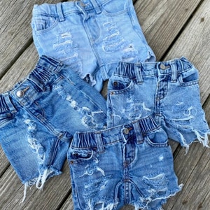 May include: Three pairs of light blue denim shorts with distressed detailing and frayed edges.