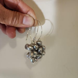 May include: A pair of silver hoop earrings with a cluster of gray pearls hanging from each hoop.