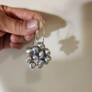 May include: Silver hoop earrings with a cluster of gray pearls hanging from the bottom.