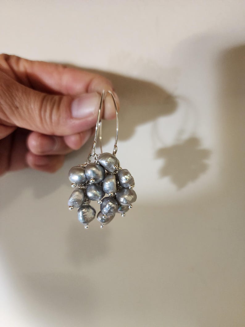 May include: Silver hoop earrings with a cluster of gray pearls hanging from the bottom.