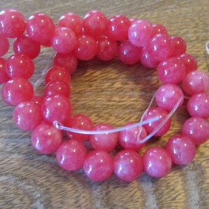 May include: A strand of pink gemstone beads, strung on a clear elastic cord. The beads are round and have a slightly translucent appearance.