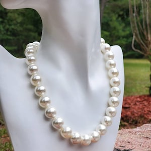 May include: A white pearl necklace with large, round pearls. The necklace is on a white mannequin bust.