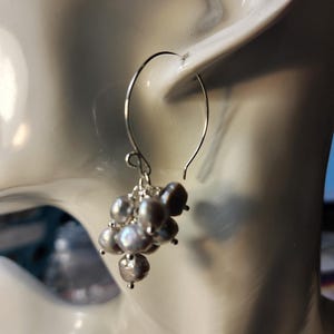 May include: Silver hoop earrings with a cluster of gray pearls hanging from the bottom.