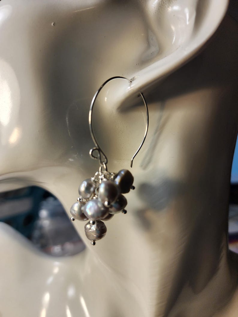 May include: Silver hoop earrings with a cluster of gray pearls hanging from the bottom.