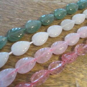 May include: A strand of gemstone beads in three colours: green, white, and pink. The beads are shaped like leaves and are strung on a clear thread.