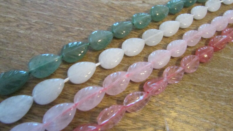 May include: A strand of gemstone beads in three colours: green, white, and pink. The beads are shaped like leaves and are strung on a clear thread.