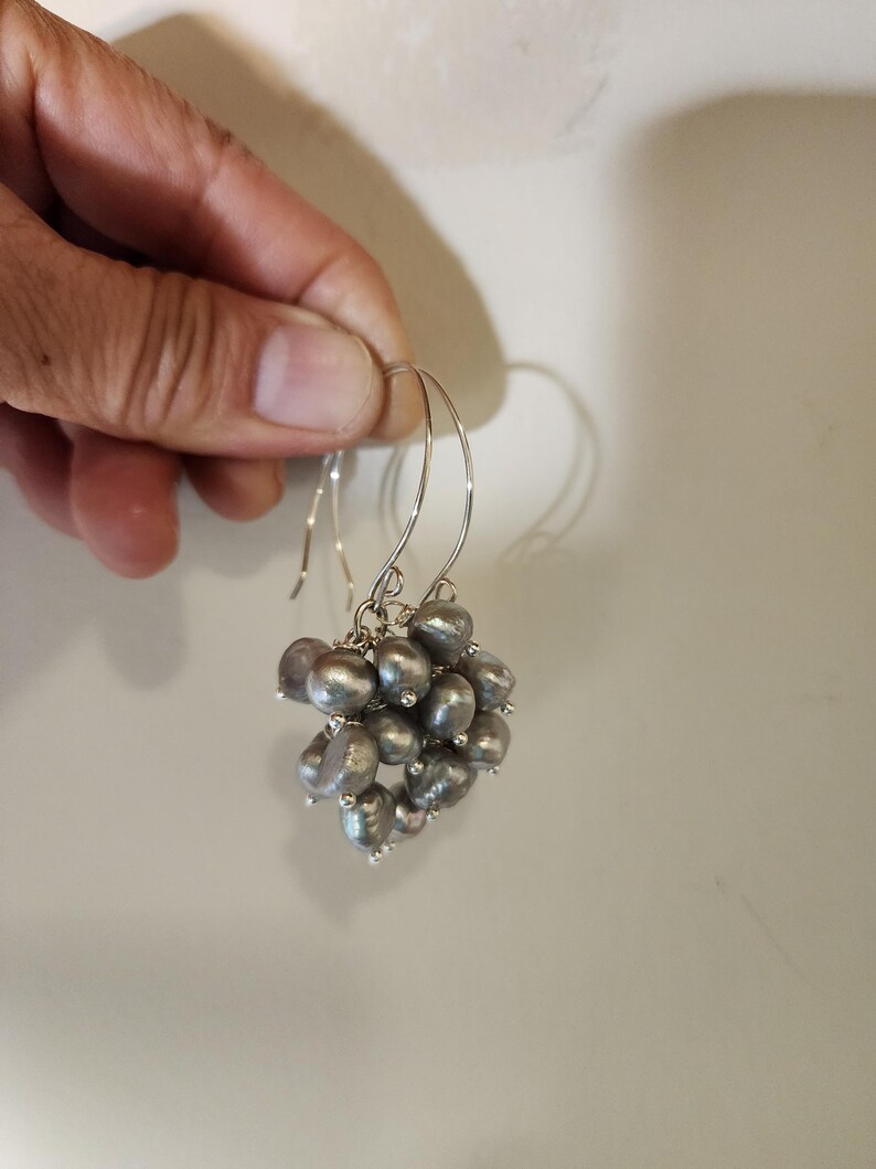 May include: A pair of silver hoop earrings with a cluster of gray pearls hanging from each hoop.