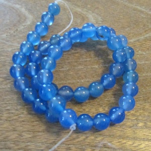 May include: A strand of light blue round beads made of agate. The beads are strung on a white thread.