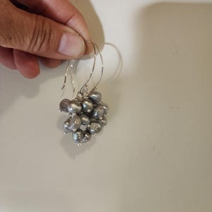May include: A pair of silver dangle earrings with a cluster of gray pearls.