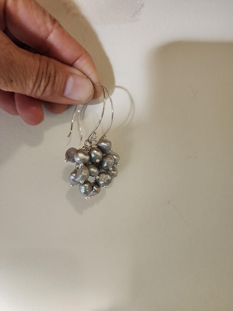 May include: A pair of silver dangle earrings with a cluster of gray pearls.