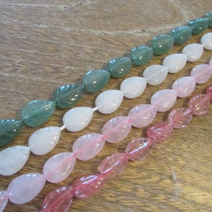 May include: A strand of gemstone beads in three colours: green, white, and pink. The beads are shaped like teardrops with a leaf design carved into them.