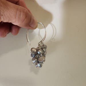 May include: Silver hoop earrings with a cluster of gray pearls dangling from the bottom.