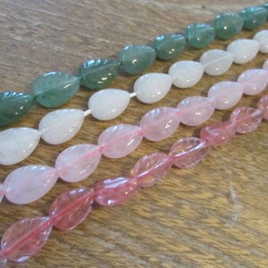 May include: A strand of light green, white, and pink gemstone beads. Each bead is shaped like a teardrop with a leaf design.