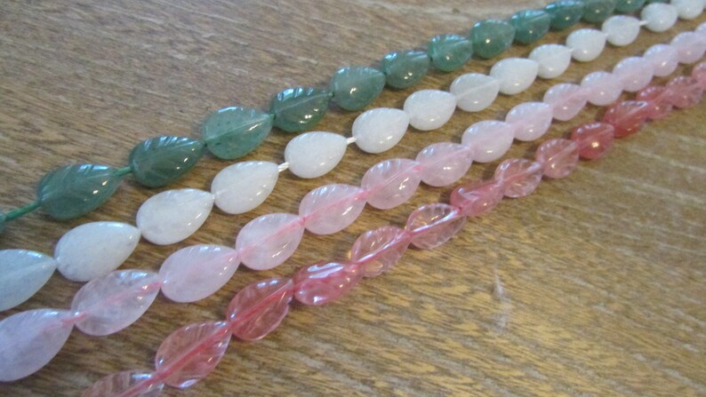 May include: A strand of light green, white, and pink gemstone beads. Each bead is shaped like a teardrop with a leaf design.