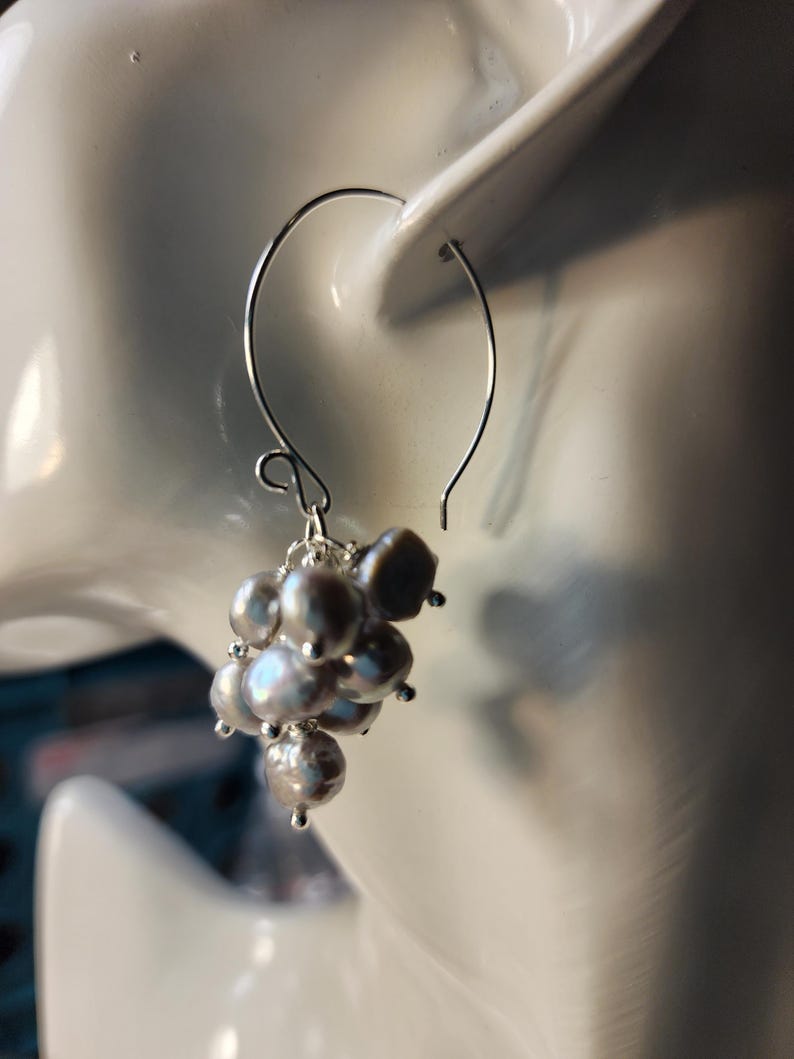 May include: Silver dangle earrings with a cluster of gray pearls.