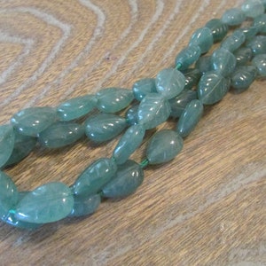 May include: A strand of light green gemstone beads, each bead is carved with a leaf design.