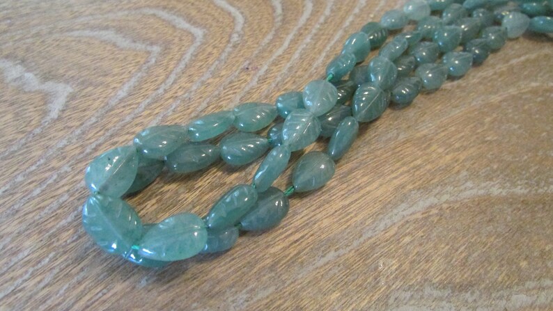 May include: A strand of light green gemstone beads, each bead is carved with a leaf design.