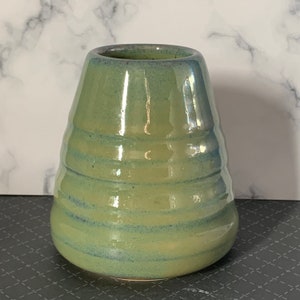 May include: A green ceramic vase with a flared opening and a rounded base. The vase has a light green glaze with darker green stripes.