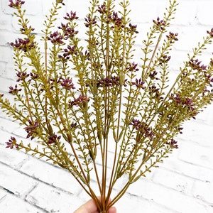 May include: A bunch of artificial purple flower stems with green leaves. The stems are bundled together and are ready to be used in a floral arrangement.