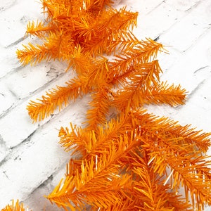 May include: Orange tinsel garland, a festive decoration for the holidays. The garland is made of thin, wispy strands of orange tinsel, creating a fluffy and whimsical look.