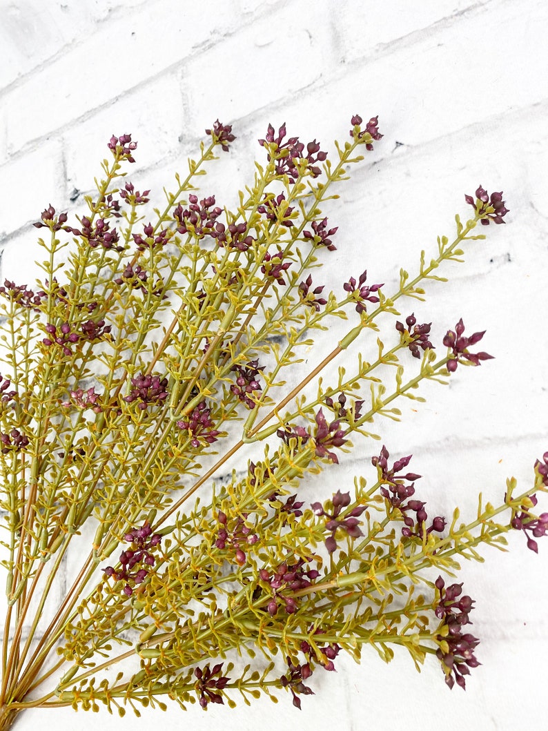 May include: A bunch of artificial greenery with small purple flower buds. The stems are green and the leaves are a light green color.