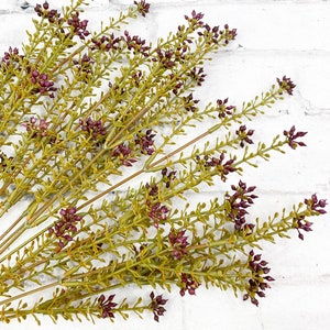 May include: A bunch of artificial greenery with small purple flowers. The stems are green and the leaves are a light green color.